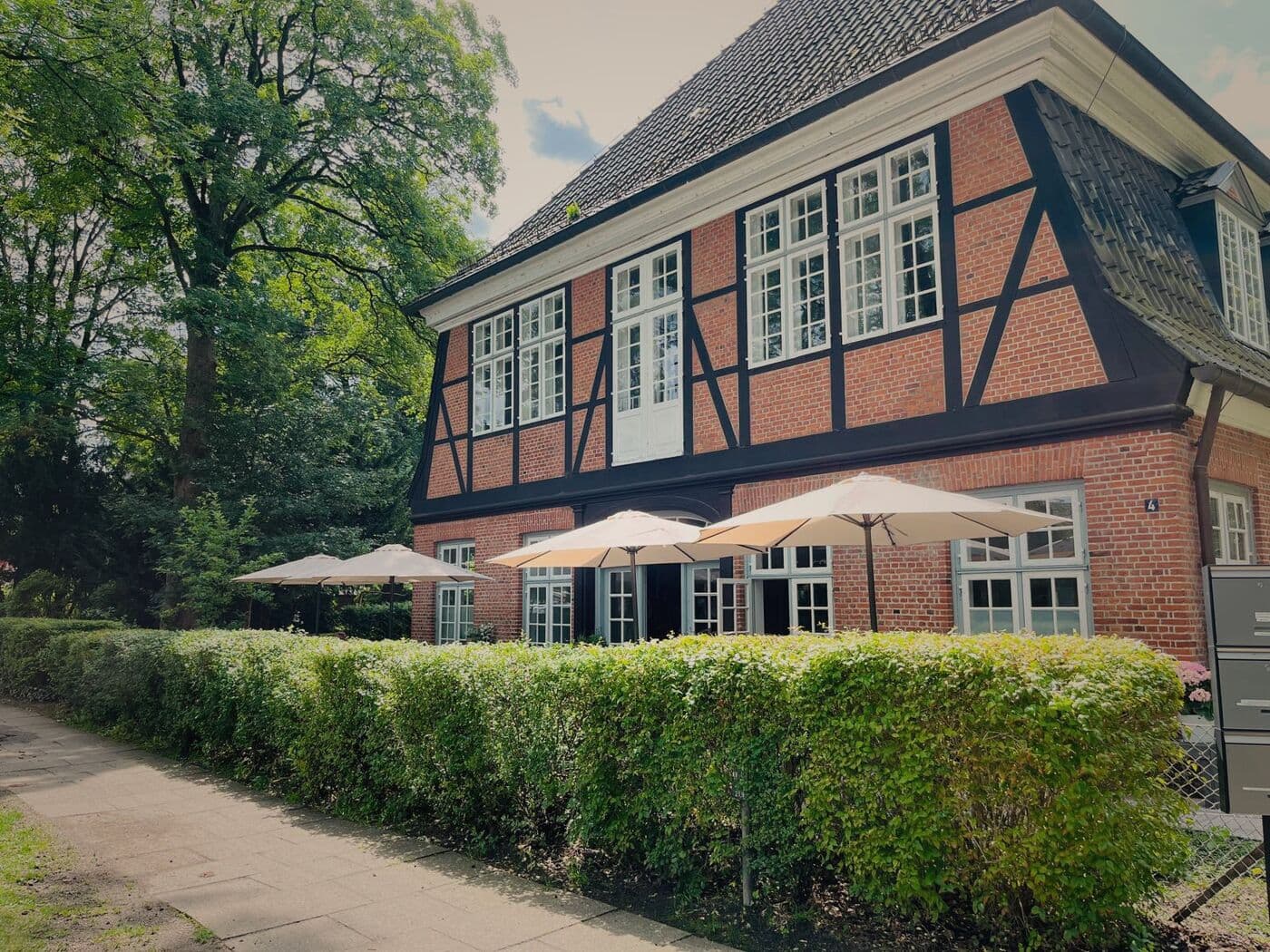 Fachwerkfassade des Stavenhagenhauses mit Sonnenschirmen hinter der Hecke