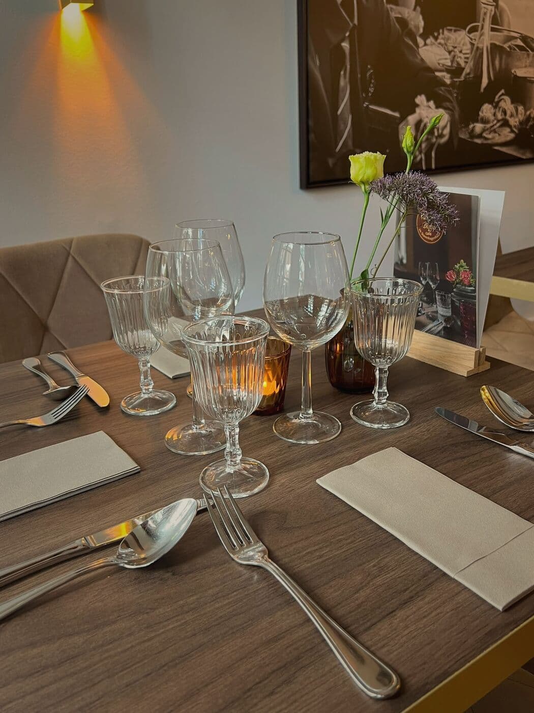 Gedeckter Tisch mit Gläsern und Blumen, dahinter Messing-Wandleuchte und Schwarz-Weiß-Bild